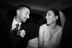 Black & White photo of a wedding couple in a car smiling at each other